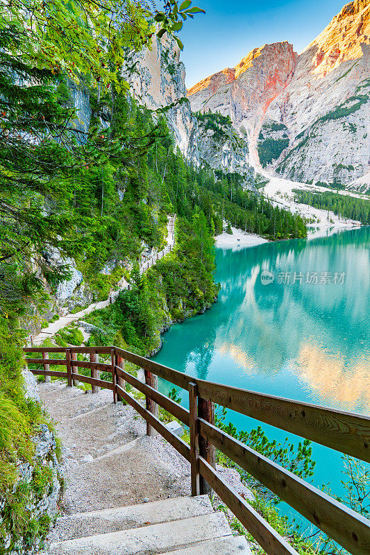 原始绿松石湖“Lago de braies”的壮丽景色，周围环绕着崎岖的山脉和郁郁葱葱的绿色植物，从有木栅栏的人行道上拍摄。